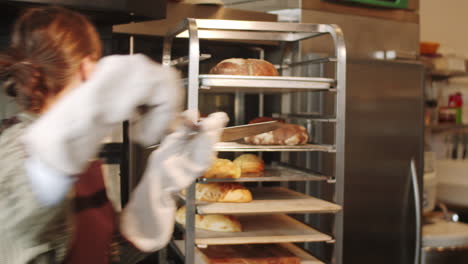 Frau-Nimmt-Brot-Mit-Schaufel-Aus-Dem-Ofen,-Während-Sie-In-Der-Bäckerei-Arbeitet